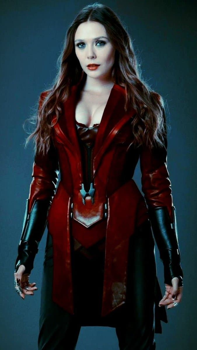 A woman with long brown hair is shown from the waist up, wearing a red leather jacket over a dark outfit. She is standing against a dark background.