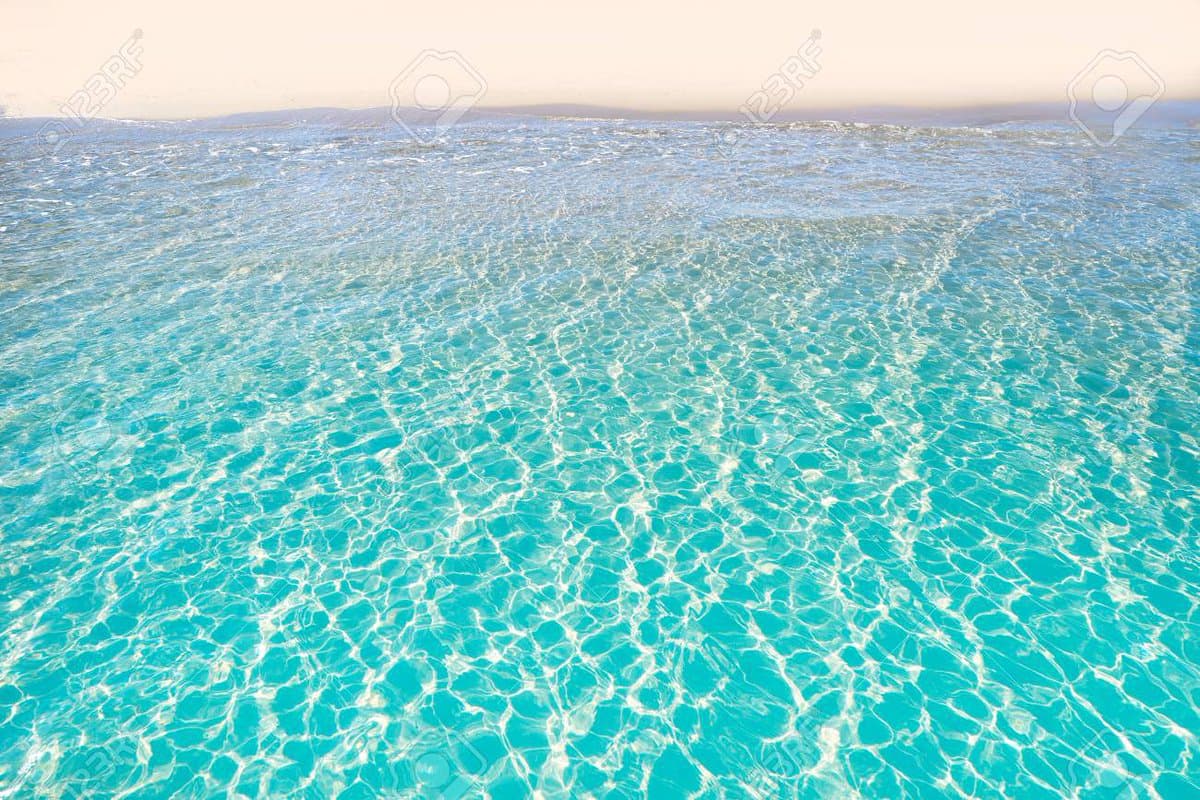 A wide-angle photograph of clear, turquoise ocean water with gentle ripples and a distant, hazy horizon line under a pale sky. The image is a stock photo, indicated by faint watermarks across the surface.