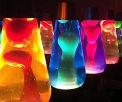 A row of colorful, illuminated lava lamps glowing in red, orange, blue, and purple against a dark background. The lamps have a classic hourglass shape with visible wax blobs suspended in liquid.