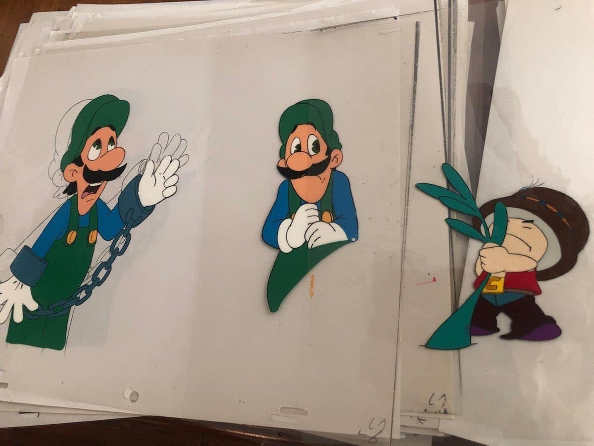 A photograph of several sheets of paper featuring hand-drawn, cutout illustrations of classic video game characters, including two depictions of Luigi and one of a character carrying a plant.