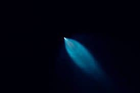 A long-exposure photograph of a bright blue light streak against a dark background, likely a meteor or satellite trail.