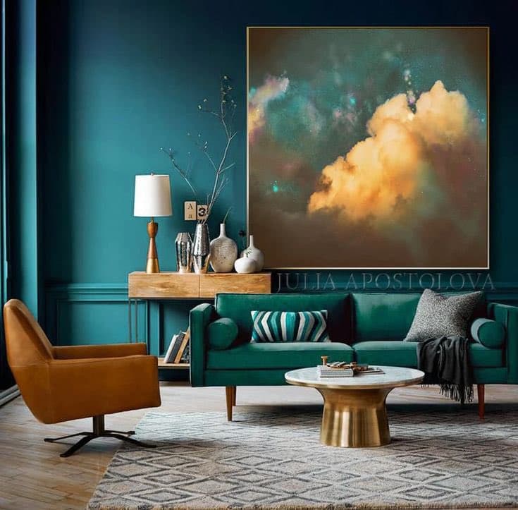 A modern living room interior featuring a teal sofa, a mustard-yellow armchair, and a large framed canvas print of a colorful nebula on the wall. The room is decorated with a wooden sideboard, a marble coffee table, and various decorative items.