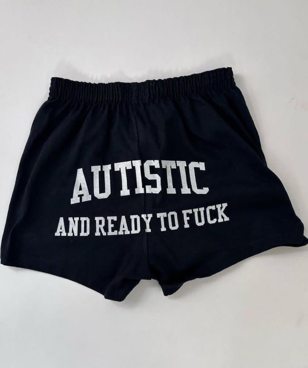 A pair of black athletic shorts laid flat on a white surface, featuring white text printed on the front. The shorts have an elastic waistband and a loose, short cut.
