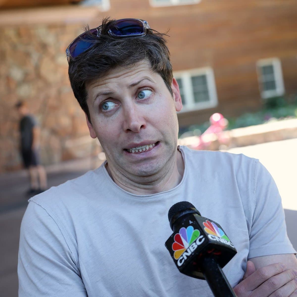 A man with sunglasses on his head makes a comically distressed facial expression while holding a CNBC microphone, set against a blurred outdoor background.