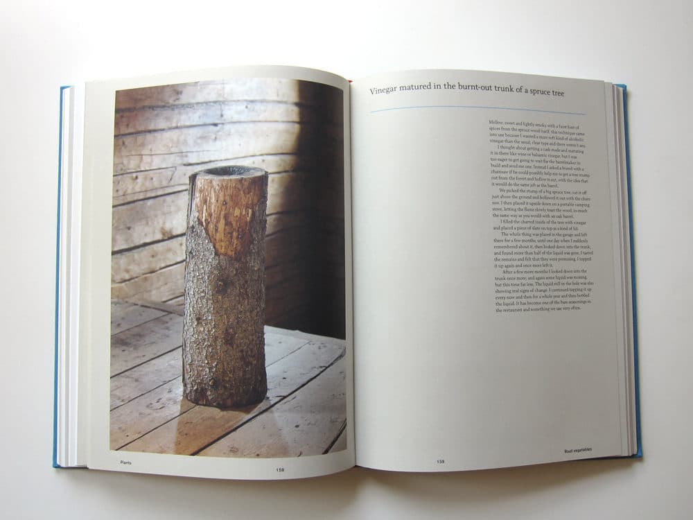 An open book displaying a two-page spread. The left page features a photograph of a hollowed-out tree trunk standing on a wooden floor, while the right page contains a text passage titled "Vinegar matured in the burnt-out trunk of a spruce tree."