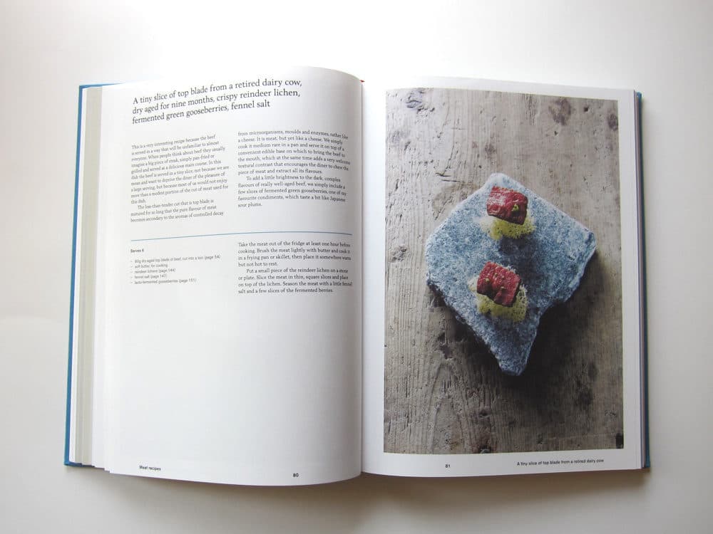 An open cookbook spread featuring a recipe for a tiny slice of top blade from a retired dairy cow, accompanied by a photograph of the dish served on a blue, textured ceramic plate.