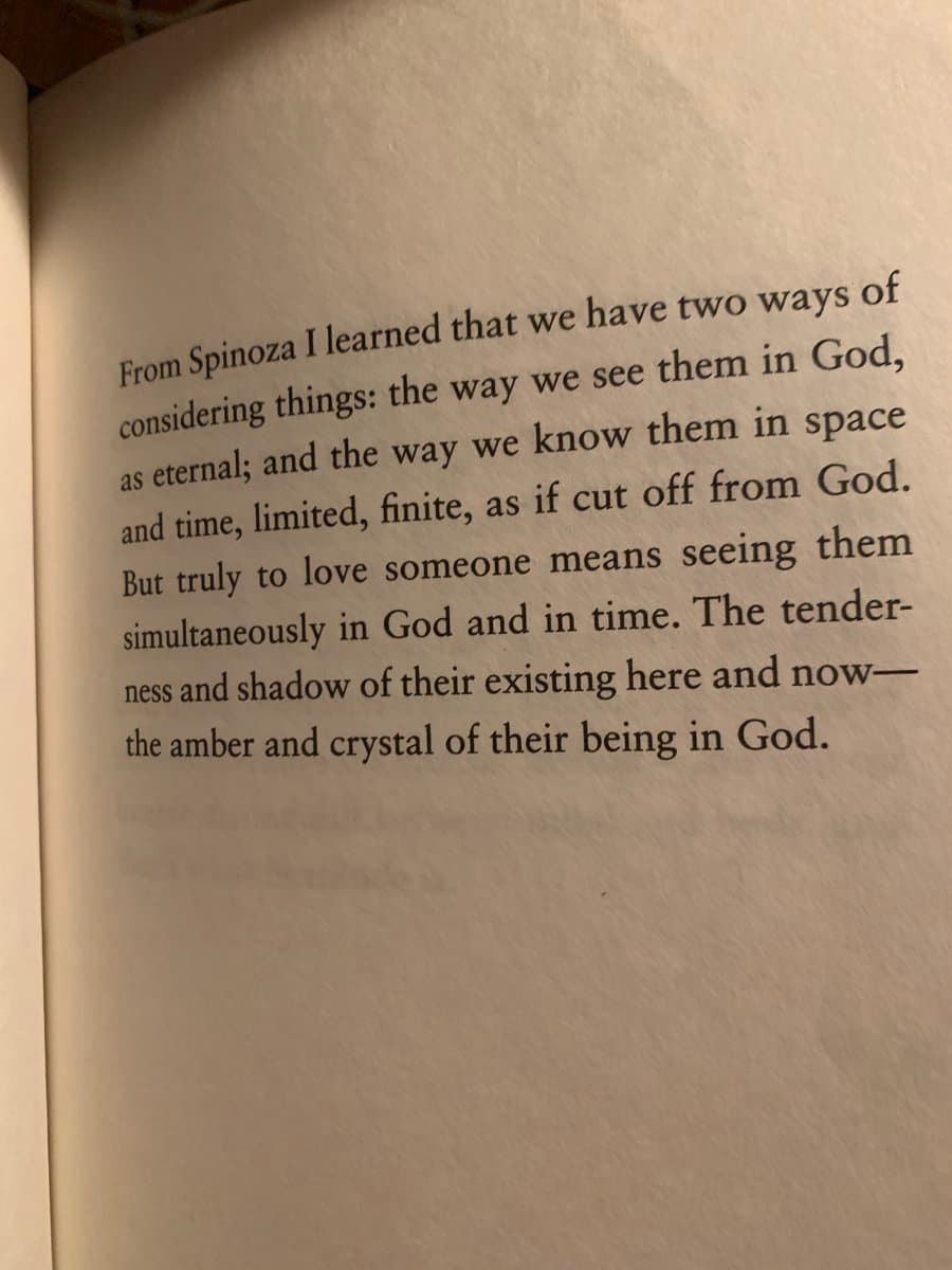A photograph of an open book page displaying a paragraph of text. The text discusses philosophical concepts related to Spinoza, God, and the nature of love and existence.