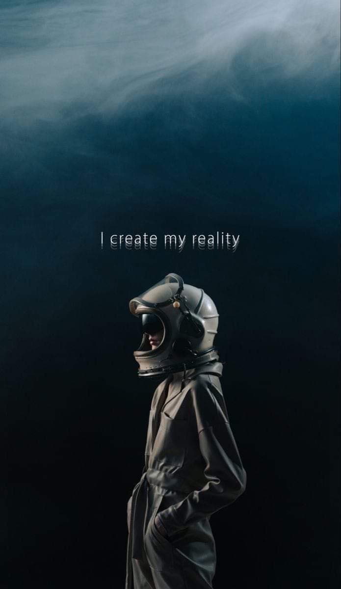 A person in a vintage-style astronaut suit and helmet stands in profile against a dark, smoky background. The text "I create my reality" is overlaid in white letters above the figure.