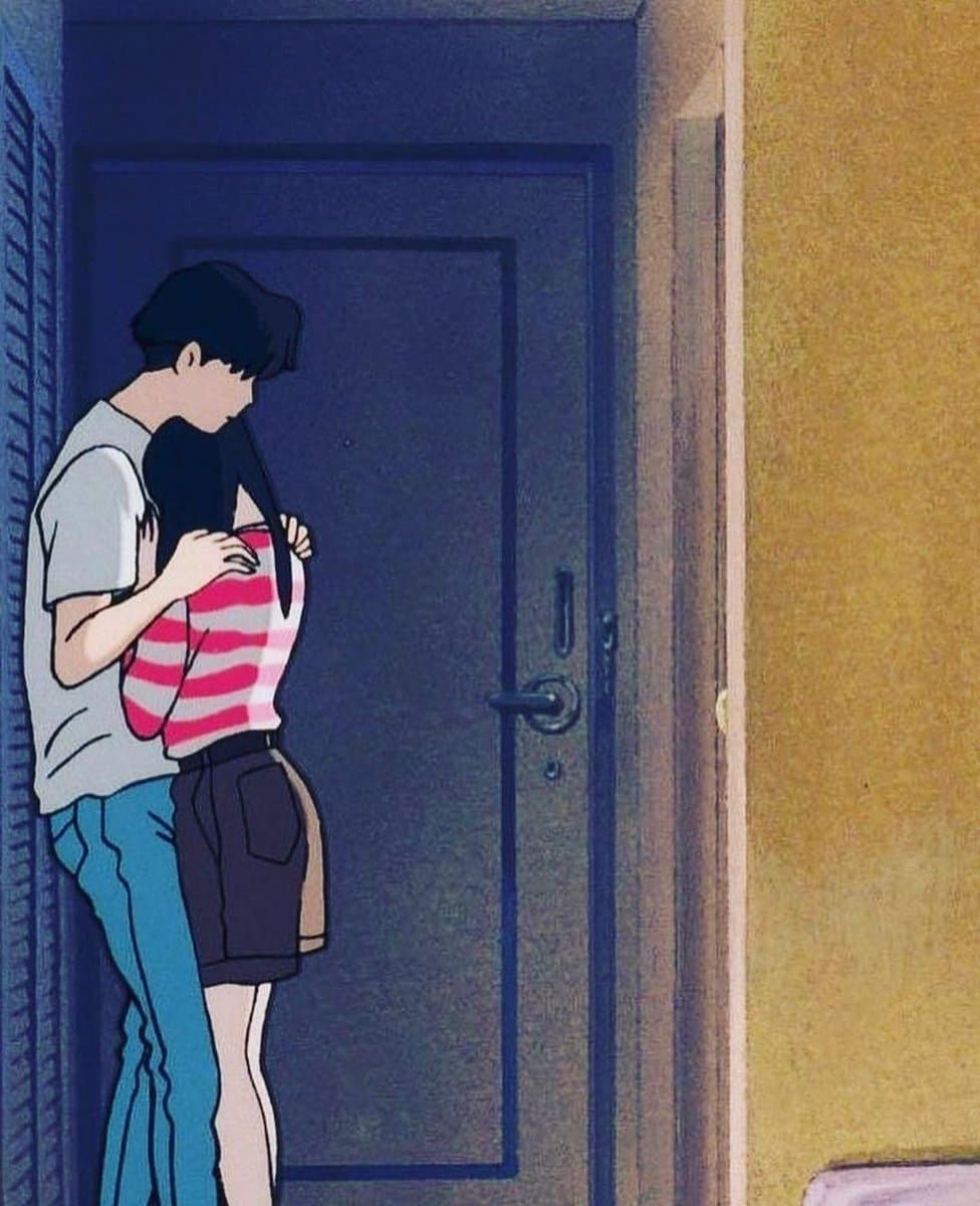 A still from the 1993 animated film 'Ocean Waves' showing a young man and woman embracing in a doorway. The man wears a white t-shirt and blue jeans, while the woman wears a pink and white striped shirt and dark shorts.
