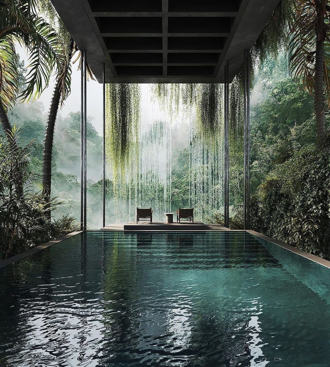 A digital rendering of a modern, open-air house interior featuring a large indoor pool that extends toward a glass wall overlooking a misty jungle. Two lounge chairs sit on a platform at the far end of the pool, facing the lush greenery outside.