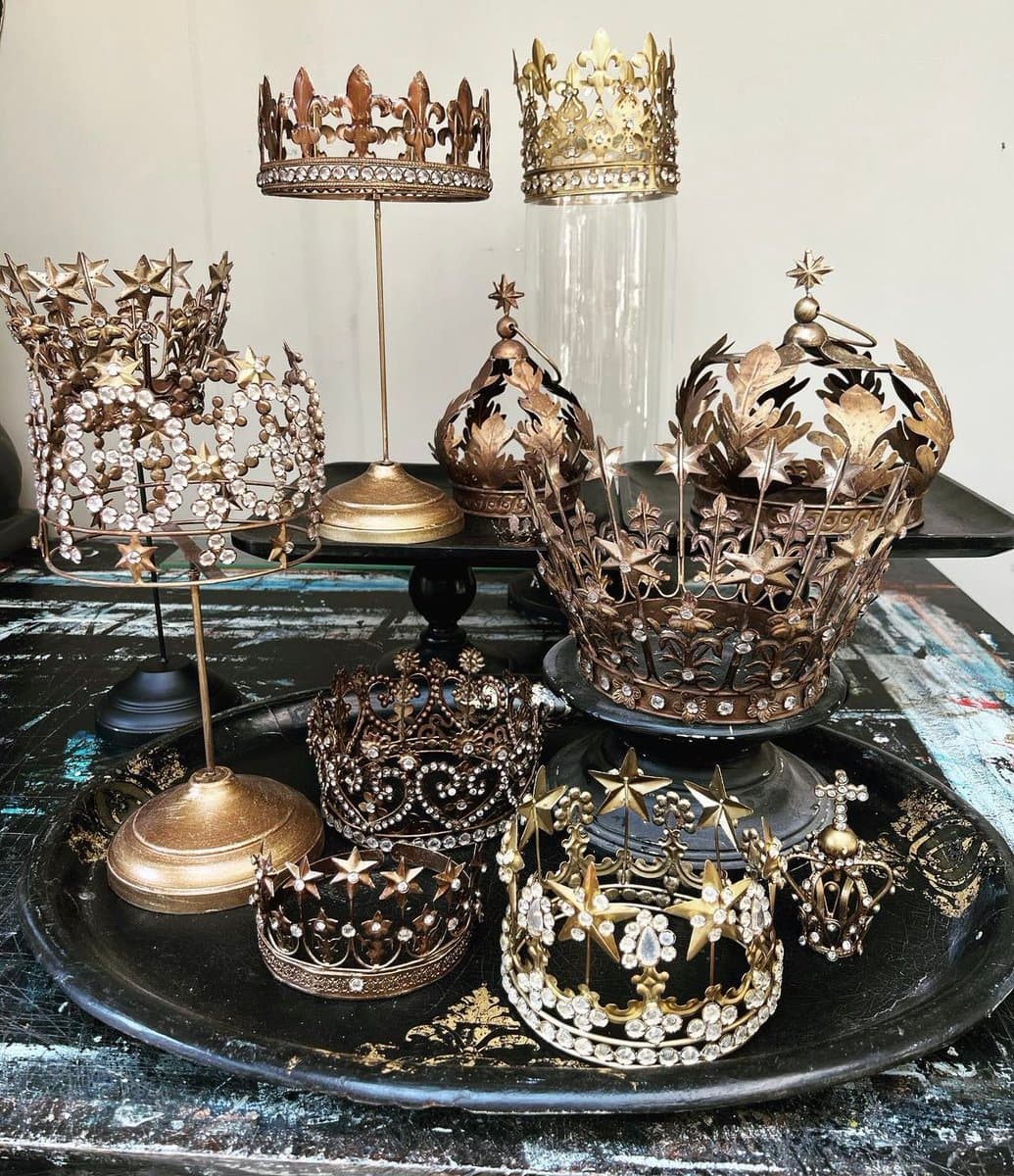 A collection of ornate, vintage-style decorative crowns and tiaras made of gold and bronze metal, featuring star and leaf motifs, displayed on stands and a black tray.