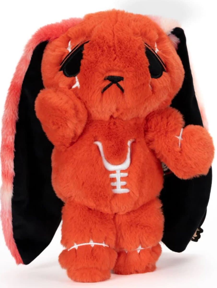 A plush toy of an orange, bat-winged creature with a sad expression, black eyes, and white stitched details on its chest, arms, and feet. The toy has long, black bat-like wings attached to its back.
