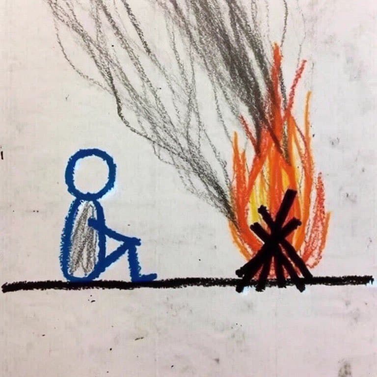 A simple, childlike drawing on white paper showing a blue stick figure sitting on a black line with its back turned toward a campfire. The fire is depicted with orange and yellow flames, black logs, and gray smoke rising upward.