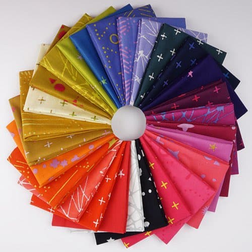 A circular fan of folded fabric swatches arranged around a central white sphere, displaying a rainbow of colors and various celestial and geometric patterns. The fabrics feature designs such as stars, moons, planets, and crosses on backgrounds ranging from deep blues and purples to bright reds, oranges, and yellows.