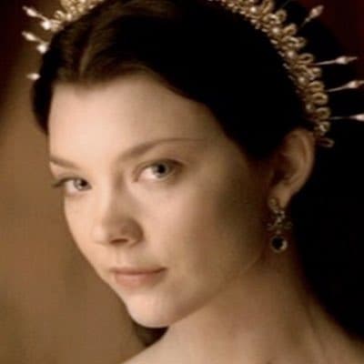 A portrait of a woman with dark hair wearing an ornate, gold-colored crown and a dark earring, set against a warm, neutral background. The image appears to be a still from a film or television show, featuring a classical or historical aesthetic. The woman is looking slightly off-camera with a calm expression.