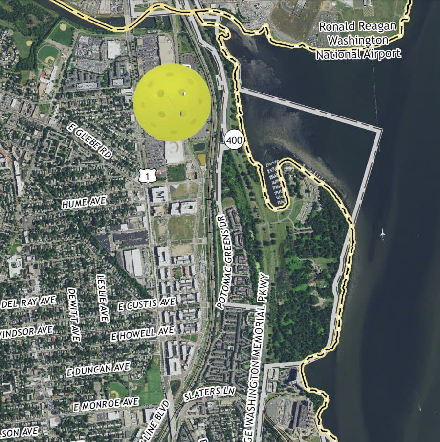 A satellite map of the Anacostia River area in Washington, D.C., showing a large yellow pickleball icon overlaid on a neighborhood near the Potomac Greens Drive and the Anacostia River. The map includes street labels, highway markers, and a highlighted boundary line along the riverbank, with Ronald Reagan Washington National Airport labeled in the upper right corner.