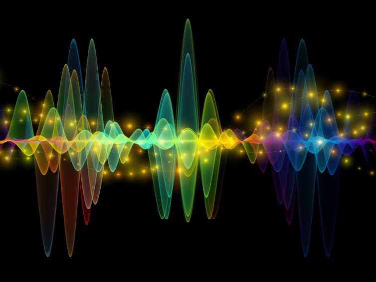 A digital illustration of a colorful, rainbow-hued sound wave with glowing yellow particles against a black background. The wave features varying amplitudes, creating a visual representation of audio frequency and volume.