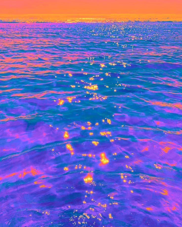 A vibrant, stylized photograph of a body of water at sunset, featuring a bright orange sky and a surface of deep purple and blue waves. The water is dotted with numerous bright, golden reflections of the sun, creating a sparkling effect across the ripples.
