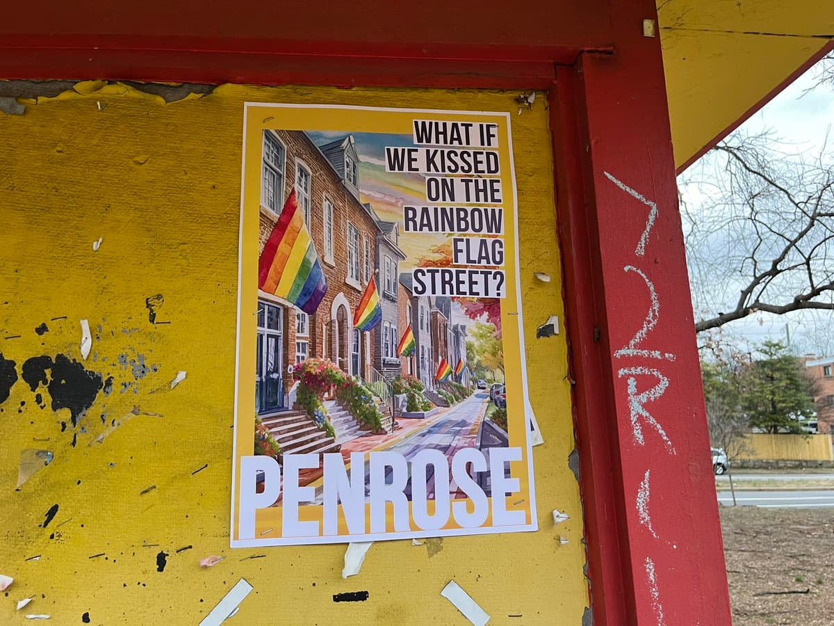 A photograph of a poster pasted on a yellow wall, featuring a painting of a residential street with rainbow flags and the word 'PENROSE' at the bottom.