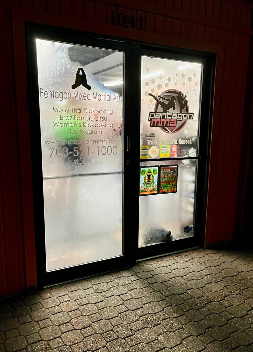 A nighttime photograph of the glass entrance doors to a martial arts studio, which are covered in condensation. The doors feature decals advertising the business's services and contact information.