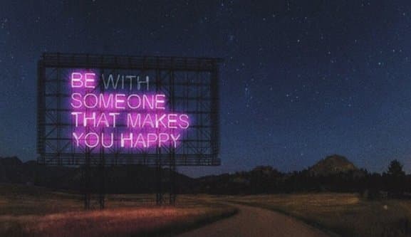A nighttime photograph of a large, illuminated billboard standing in a rural landscape under a starry sky. The billboard displays a motivational message in bright pink neon-style lettering.