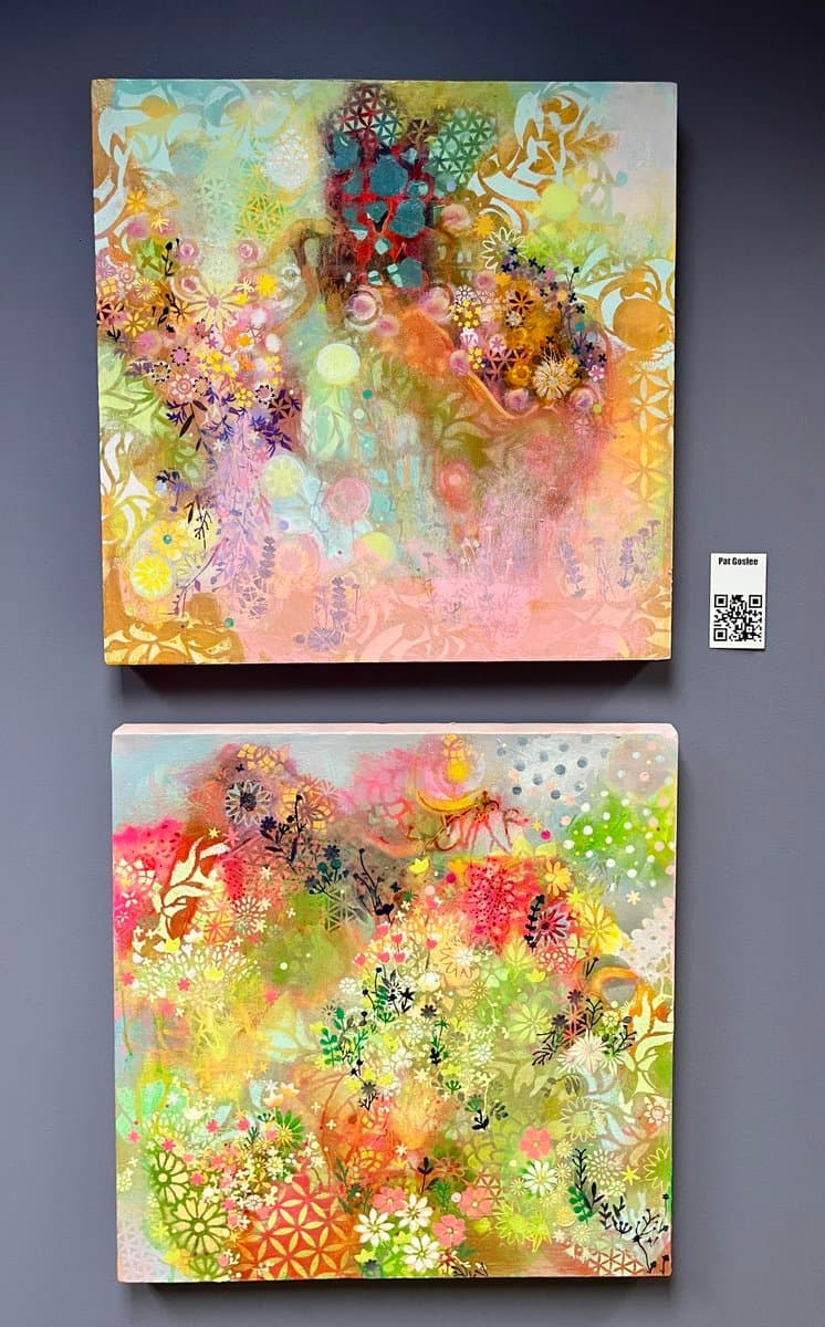 Two square abstract paintings featuring colorful floral and geometric patterns are displayed one above the other against a dark gray background. A small white label with a QR code and the name 'Pat Costee' is attached to the right side of the top canvas.
