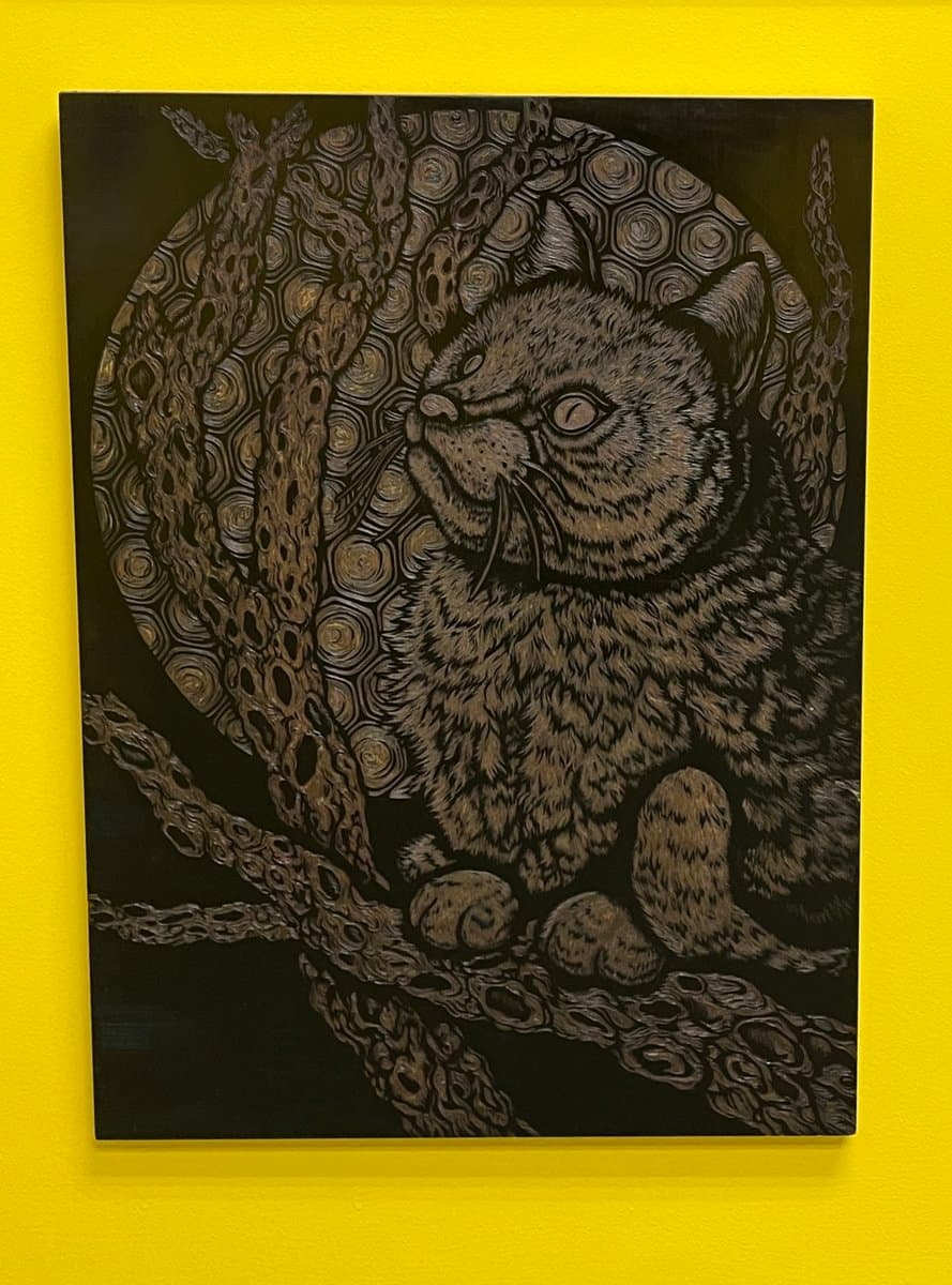 A detailed, dark-toned artwork of a cat perched on a branch, featuring intricate swirling patterns in the background, displayed on a bright yellow wall.