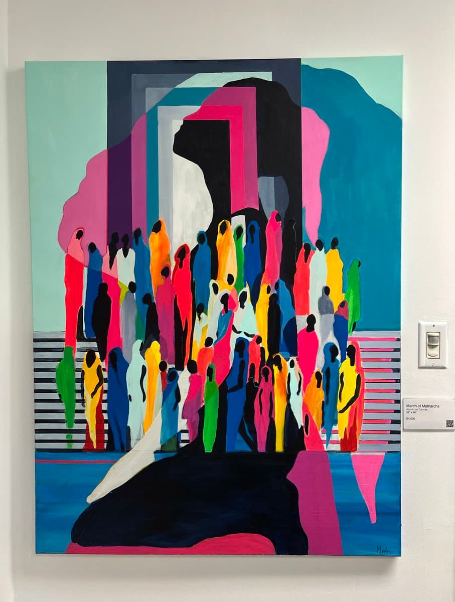 A colorful abstract painting on a gallery wall depicting a crowd of stylized, faceless figures in vibrant colors standing on a striped platform. A small gallery label is visible on the wall to the right of the artwork.