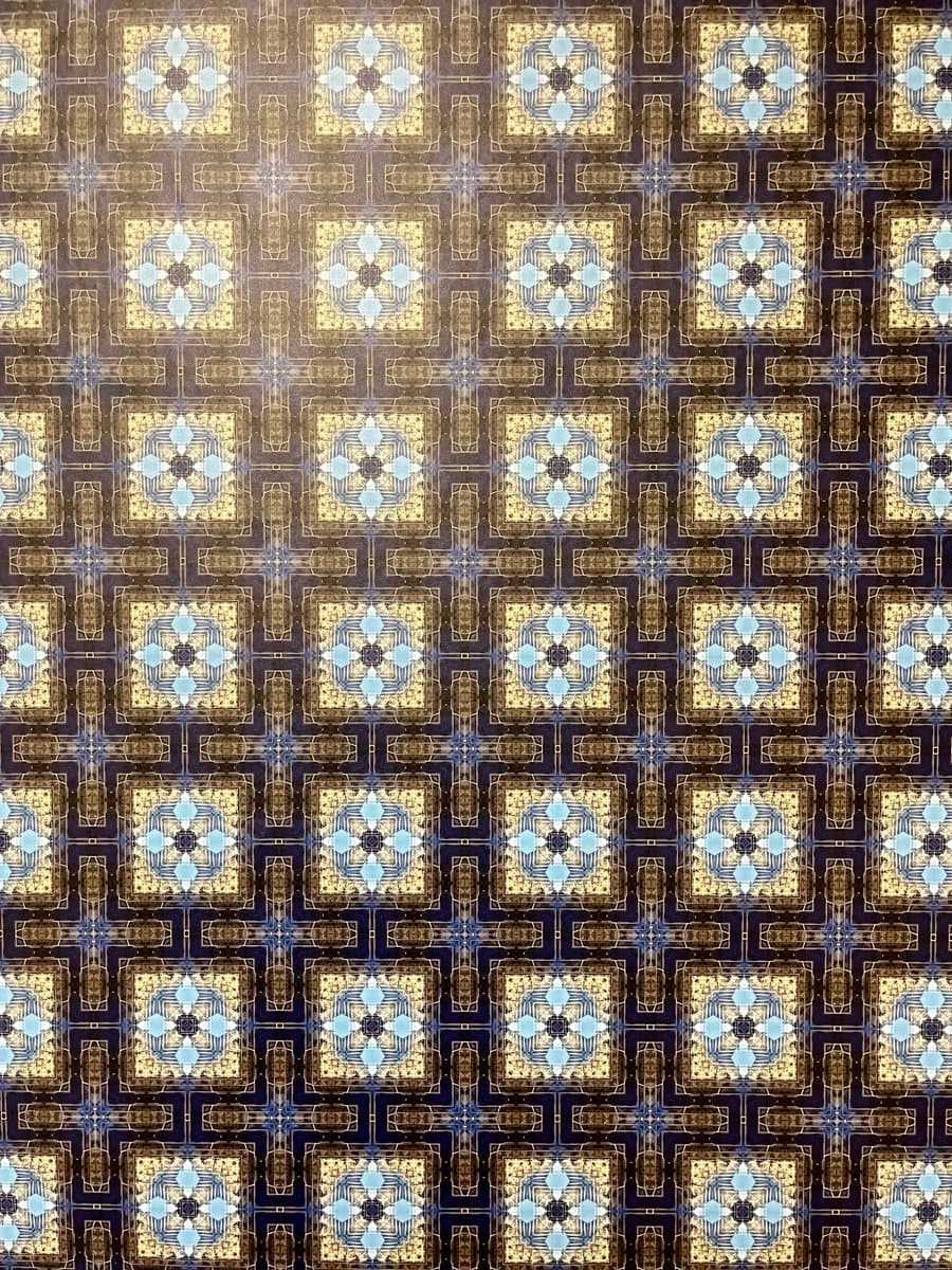 A digital image featuring a repeating, symmetrical geometric pattern in gold, blue, and white tones. The design consists of intricate, ornate square motifs arranged in a grid, resembling a decorative wallpaper or textile print.