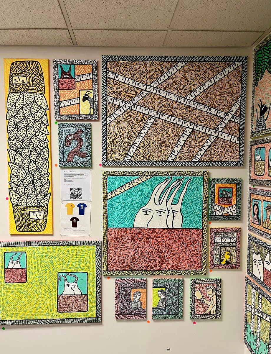 A gallery wall display featuring numerous colorful, patterned artworks in a distinctive illustrative style, including portraits and abstract figures. A printed sheet with a QR code and t-shirt designs is also pinned to the wall among the art pieces.