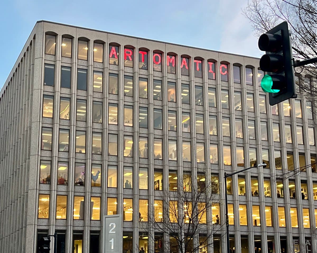 A low-angle photograph of a multi-story office building with the word "ARTOMATIC" displayed in large red letters across the top. A traffic light showing a green signal is visible in the foreground on the right.