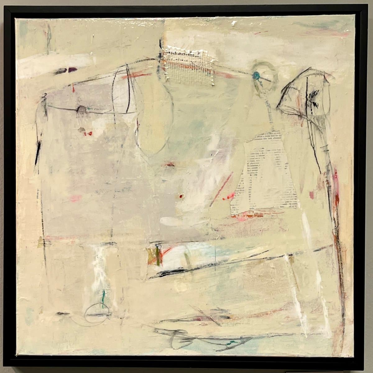 A framed abstract painting featuring a pale, textured background with loose black line drawings, faint colored accents, and a piece of printed paper collage. The artwork is displayed in a simple black frame.