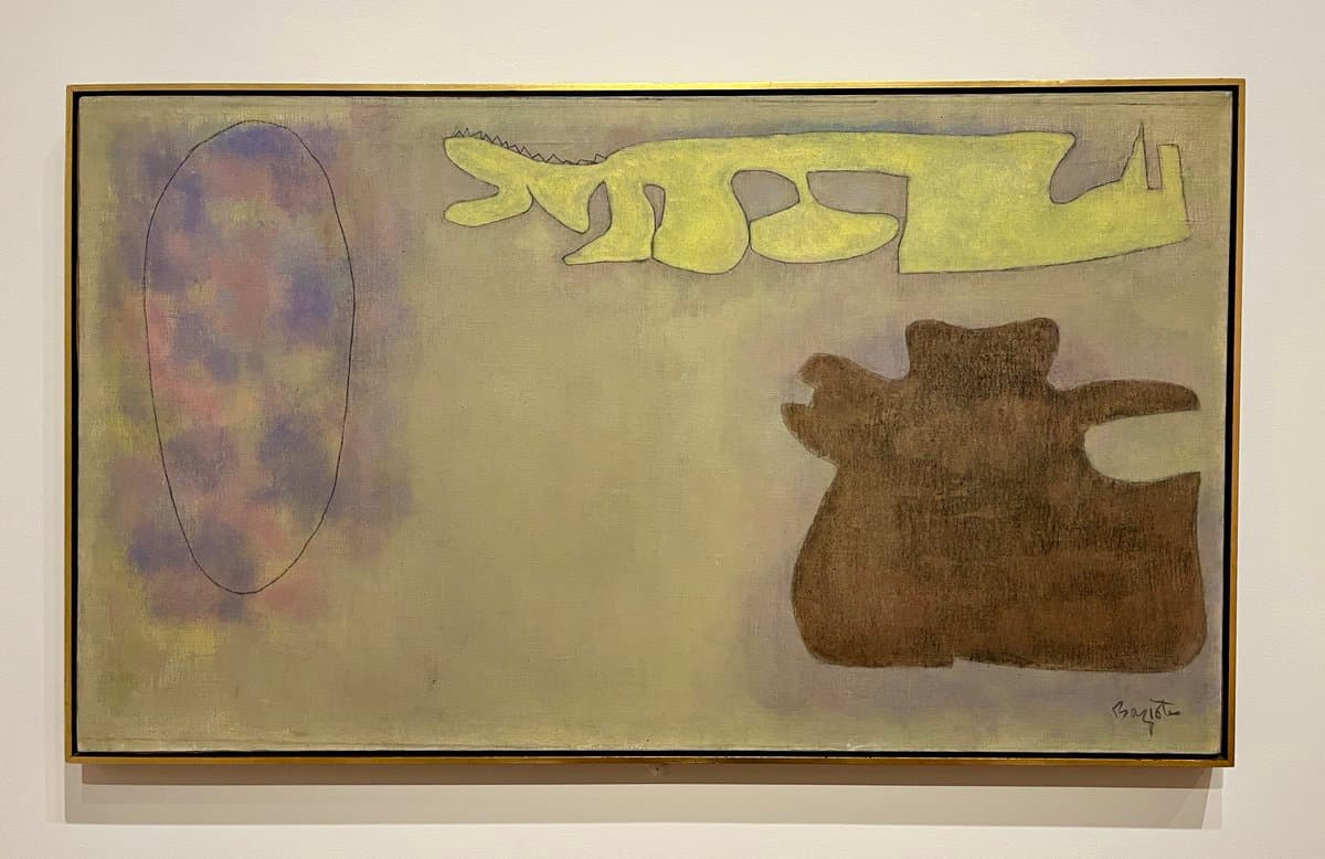 A framed abstract painting hanging on a white gallery wall, featuring a large yellow crocodile-like shape, a brown organic form, and a purple oval on a muted beige background.