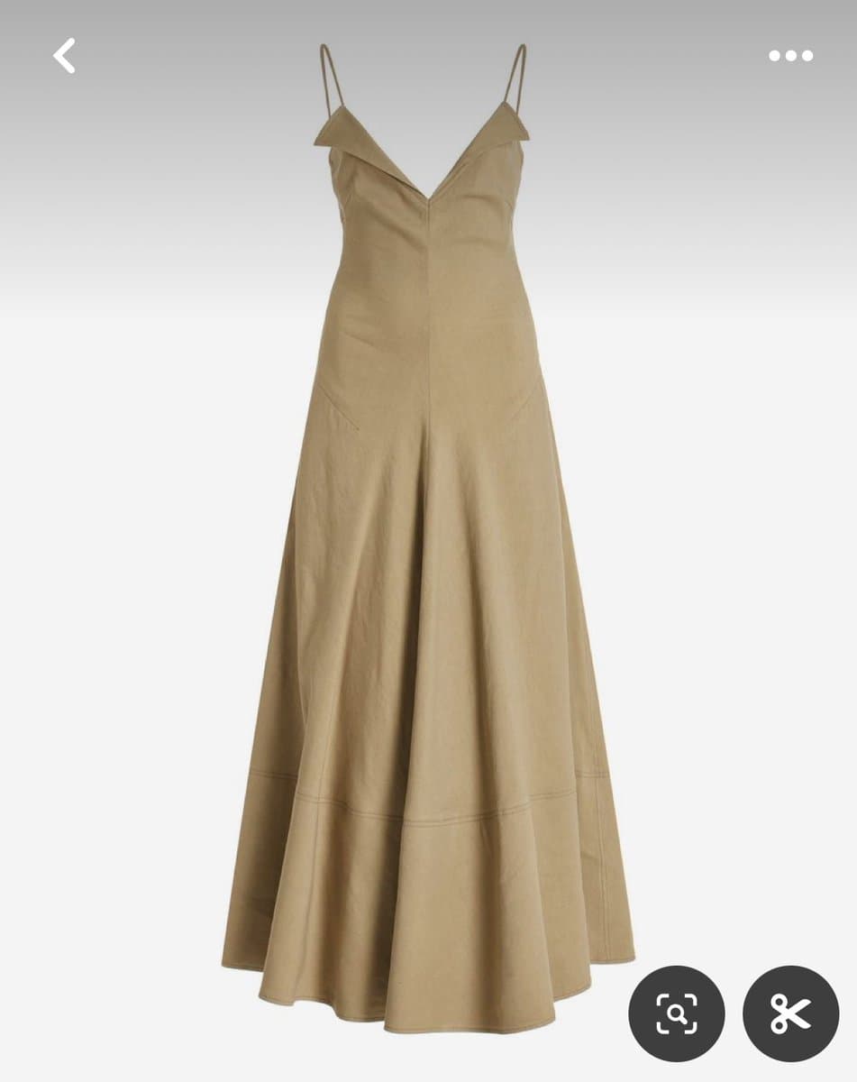 A screenshot of a Pinterest image showing a long, beige slip dress with thin straps and a V-neckline. The dress has a flowing, A-line skirt and is displayed against a plain white background with Pinterest interface icons visible at the top and bottom.