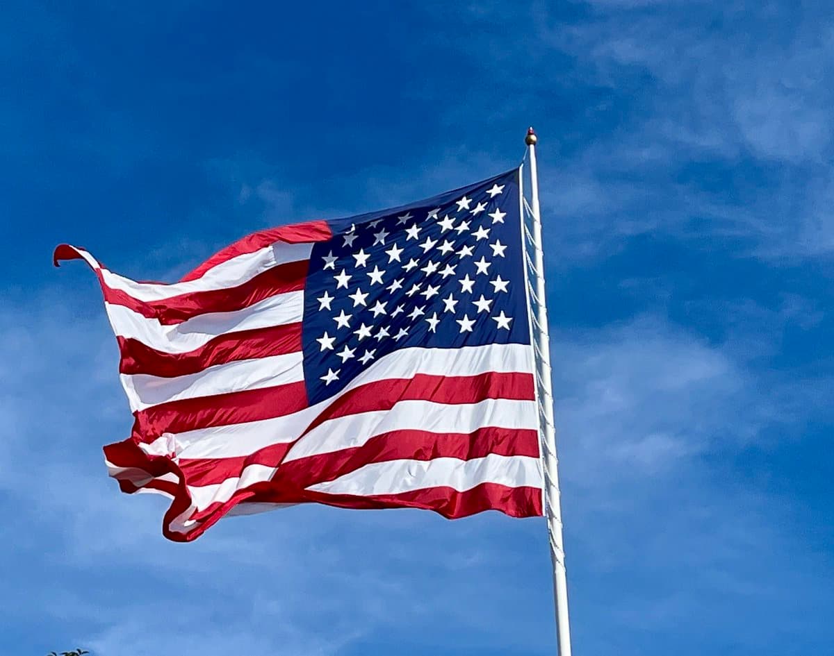 A photograph of an American flag waving on a flagpole against a blue sky with light clouds.
