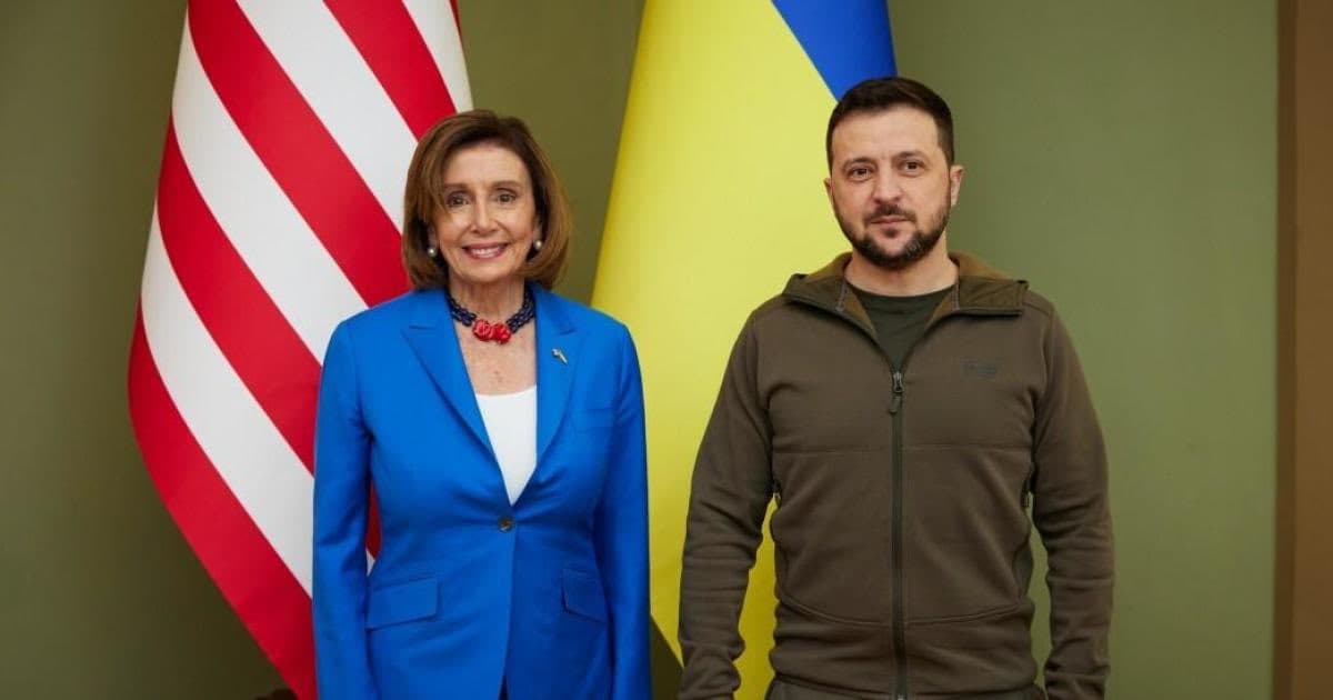 A photograph of two people standing side-by-side in front of the American and Ukrainian flags. The woman on the left wears a blue suit jacket, and the man on the right wears a brown fleece jacket.