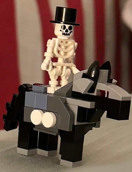 A LEGO skeleton minifigure wearing a black top hat is standing on a black and gray LEGO horse. The figure is positioned in front of a red and white striped background.