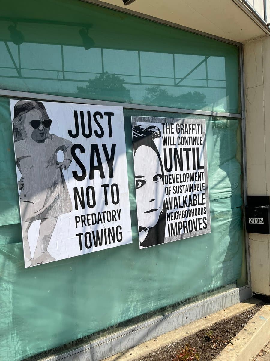 Two black-and-white protest posters are taped to a green-tinted storefront window. The left poster features a stylized figure with sunglasses and the text 'JUST SAY NO TO PREDATORY TOWING,' while the right poster shows a face and reads 'THE GRAFFITI WILL CONTINUE UNTIL DEVELOPMENT OF SUSTAINABLE WALKABLE NEIGHBORHOODS IMPROVES.'