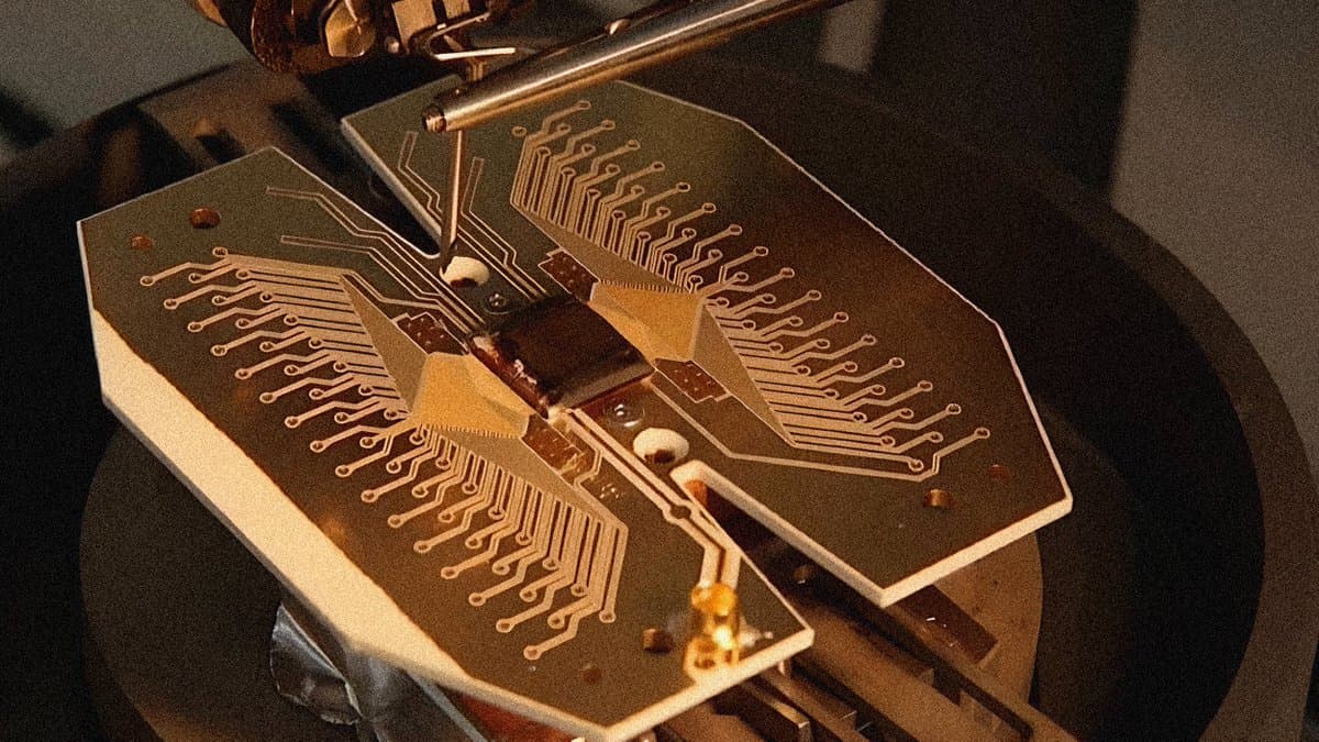 A close-up photograph of a butterfly-shaped printed circuit board (PCB) with intricate copper traces and a central component, mounted on a mechanical testing apparatus.