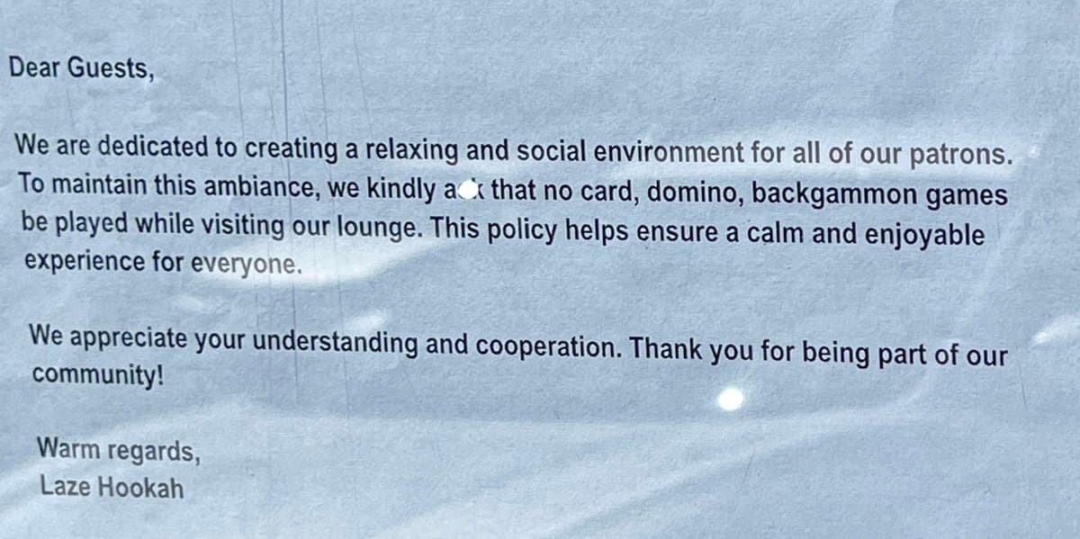 A photograph of a printed notice on white paper, likely a sign or letter from a lounge. The text explains a house policy prohibiting card, domino, and backgammon games to maintain a relaxing atmosphere.