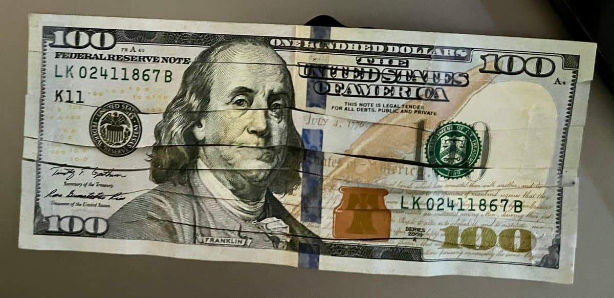 A photograph of a crumpled United States one hundred dollar bill featuring a portrait of Benjamin Franklin. The bill is marked with the serial number LK02411867B and the series year 2009.