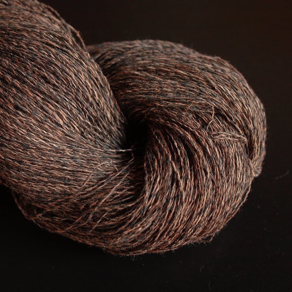 A close-up photograph of two skeins of brown, variegated yarn resting on a dark surface. The yarn has a heathered texture with shades of brown, black, and tan.