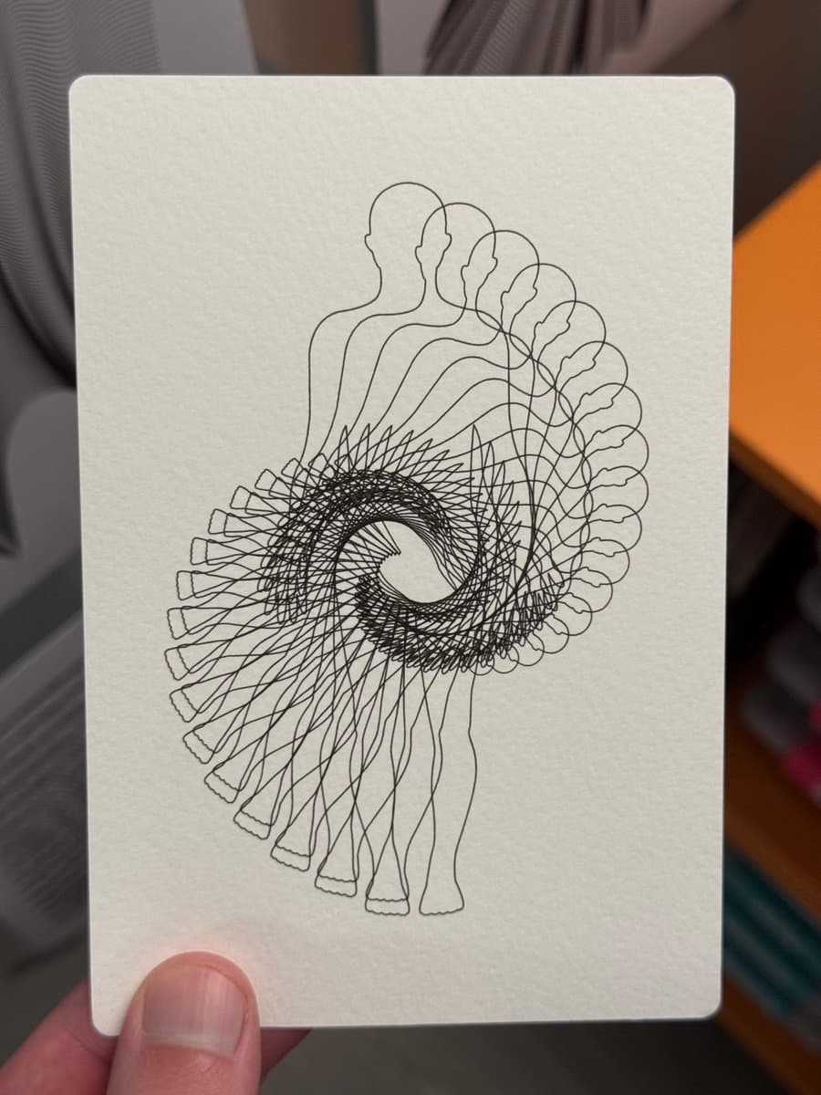 A hand holds a white card featuring a black line drawing of a human figure that appears to be twisting and dissolving into a spiral of overlapping outlines. The drawing is a continuous line illustration on a piece of paper held against an indoor background.