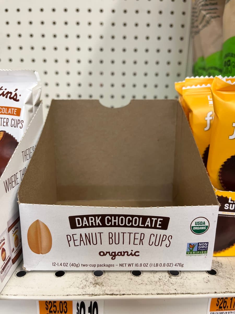 A photograph of an empty cardboard display box for 'Dark Chocolate Peanut Butter Cups' on a store shelf, with the product's packaging visible on the sides. The box is labeled 'organic' and features USDA Organic and Non-GMO Project Verified logos.