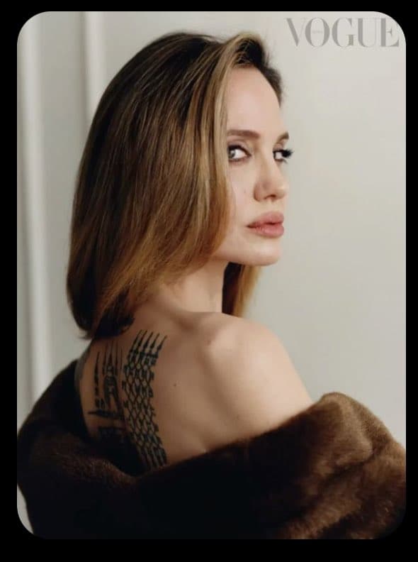 A portrait of a woman with shoulder-length brown hair looking over her shoulder, wearing a brown fur coat that reveals a tattoo on her upper back. The Vogue logo is visible in the upper right corner.