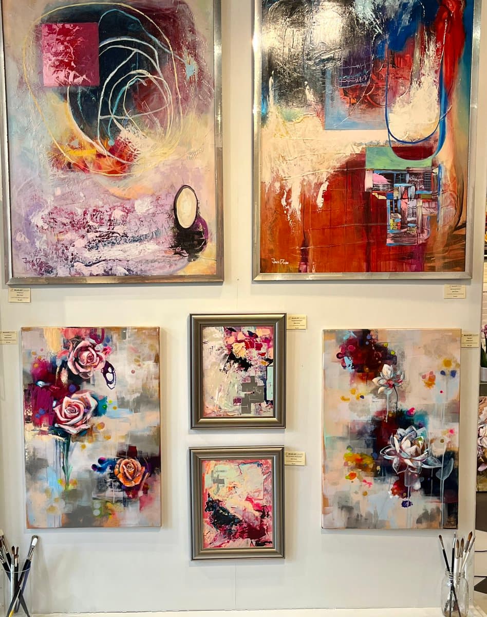 A gallery wall display featuring five framed abstract and floral paintings arranged in two rows. The top row contains two large abstract canvases, while the bottom row features a floral painting on the left, two smaller framed pieces in the center, and another floral piece on the right.