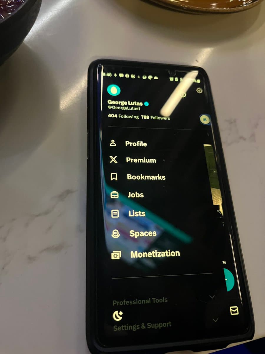 A photo of a smartphone displaying the X (formerly Twitter) app's profile menu. The screen shows the user's profile name, handle, and follower counts, along with a list of navigation options such as Profile, Premium, and Monetization.
