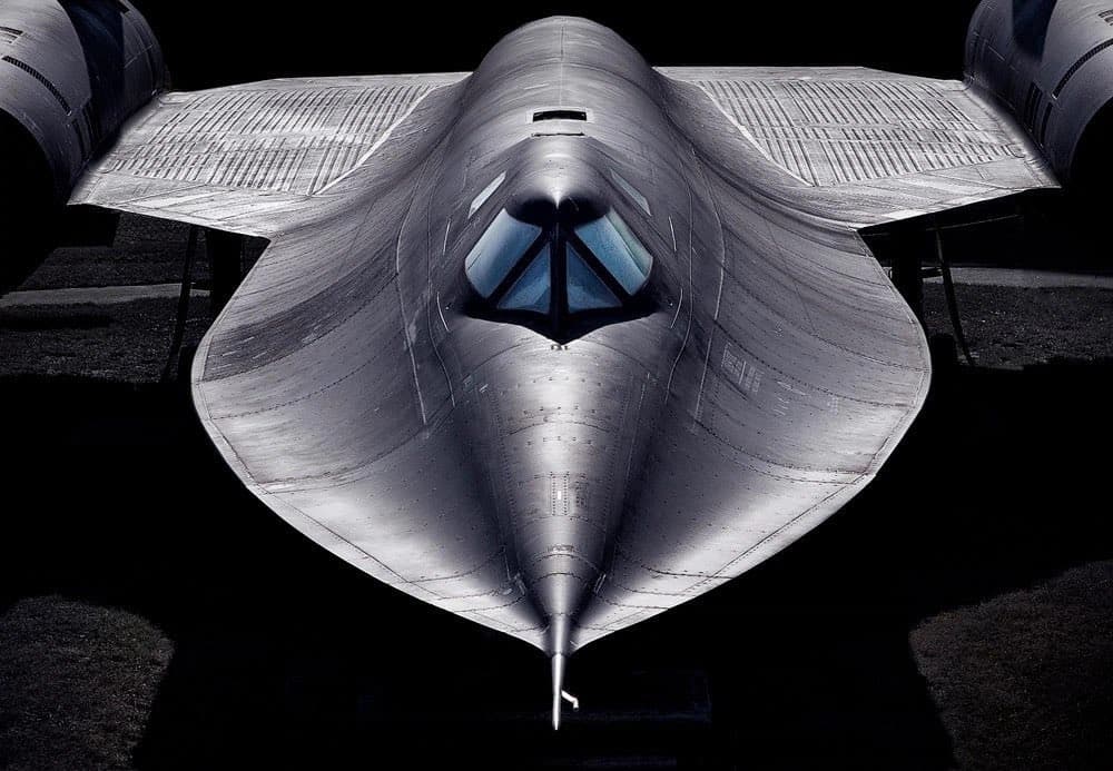 A front-facing, high-contrast photograph of a silver, delta-winged stealth aircraft, likely a Lockheed F-117 Nighthawk, set against a black background. The image highlights the aircraft's angular, faceted design and cockpit windows.