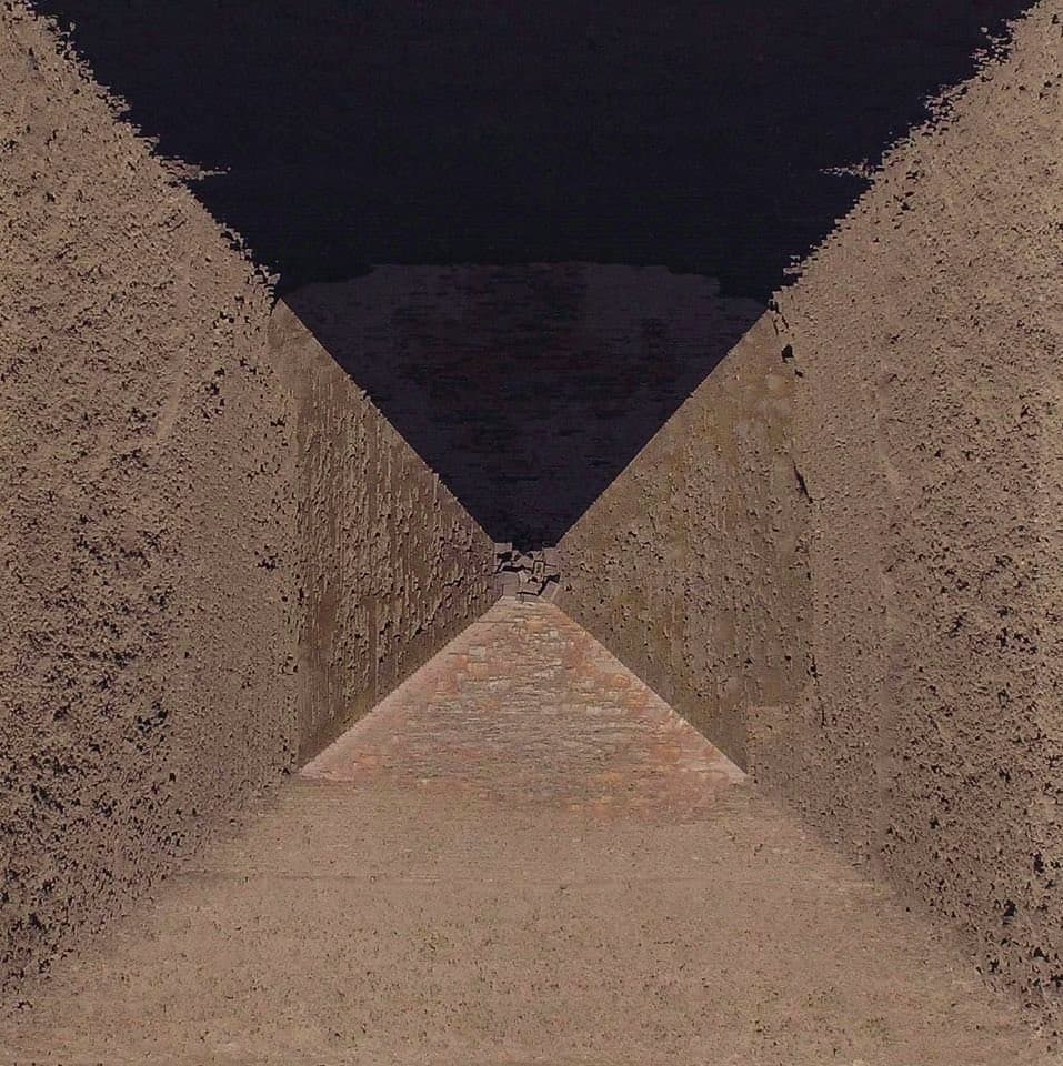 A photograph of a narrow, V-shaped stone passageway or trench with steep, textured walls converging toward a dark opening in the distance.