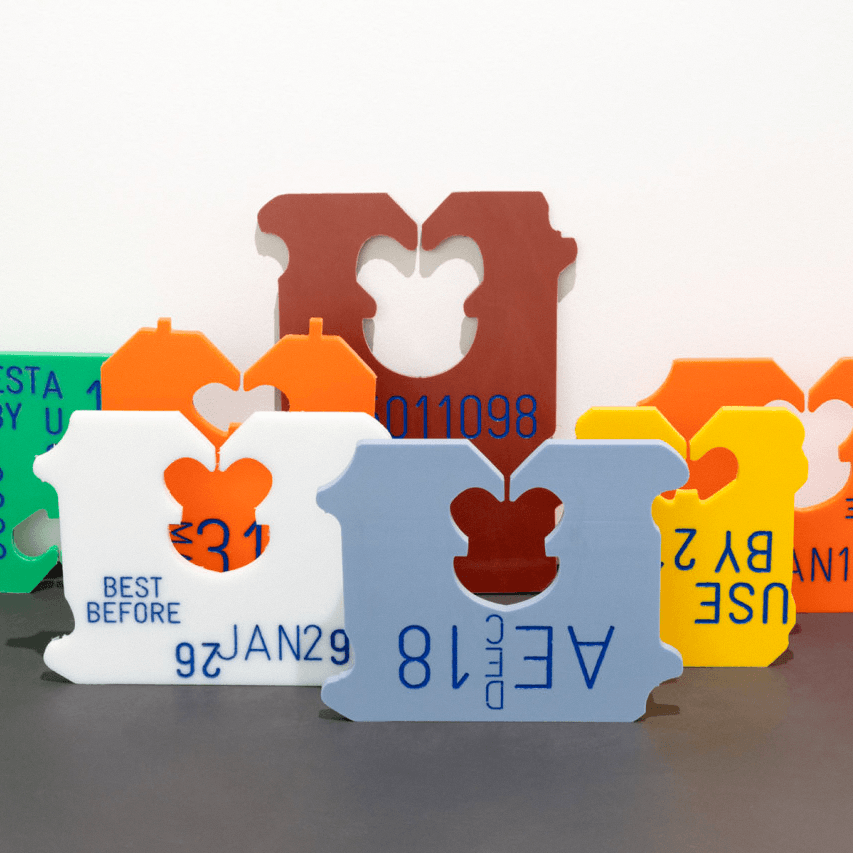A collection of colorful, interlocking plastic puzzle pieces arranged on a table, each printed with text and numbers resembling expiration dates and product codes. The pieces are designed to fit together, with some forming a larger, more complex shape in the background.